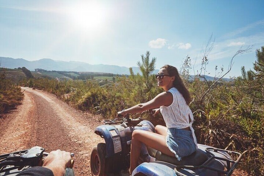 A person riding a quad bike on a dirt road with a mountainous landscape in the background. 3