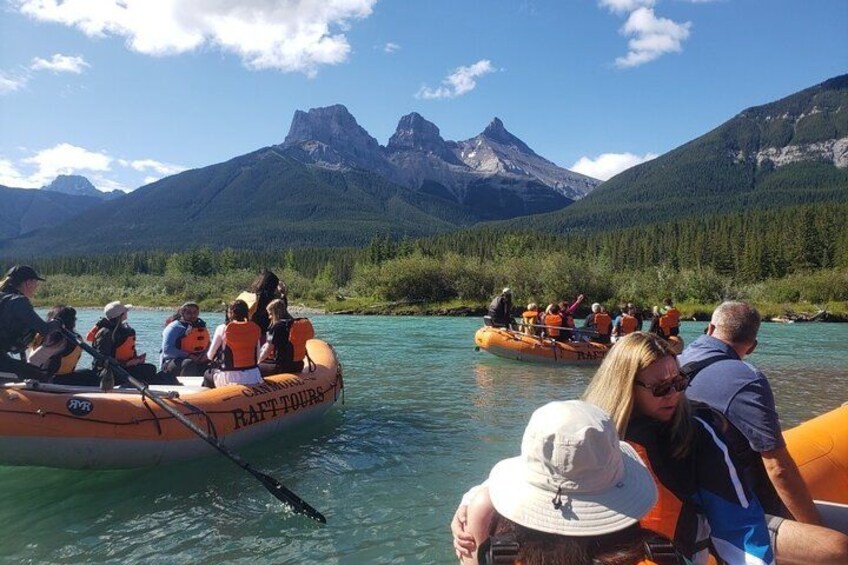 A group of people rafting on a river with mountains in the background. 2