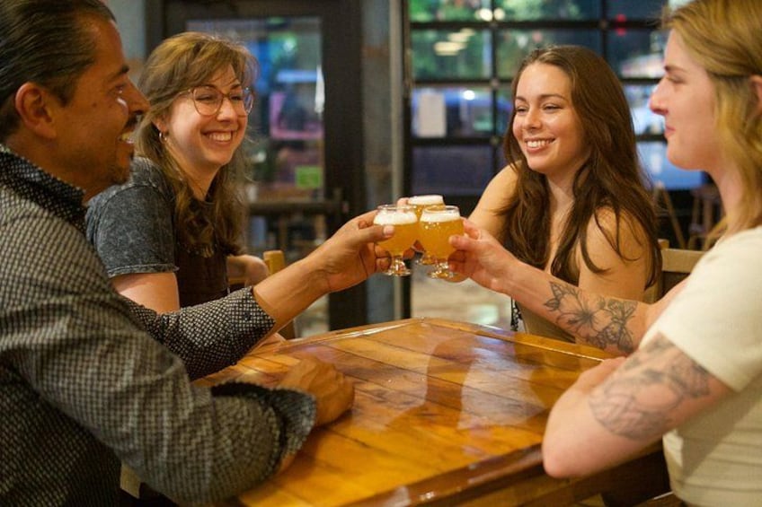 Un grupo de personas brindando con vasos de cerveza en una mesa de madera en un bar. 3