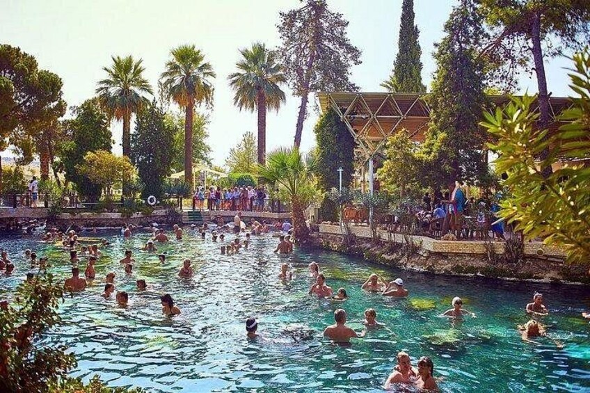 A swimming pool with people in the water, surrounded by palm trees and a building. 4