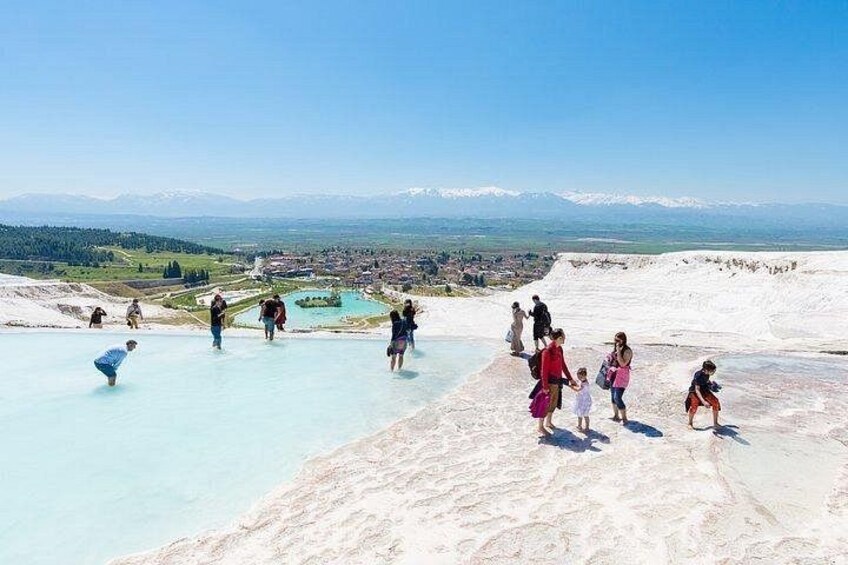 A group of people walking on a white, terraced landscape with a view of a distant town and mountains. 1