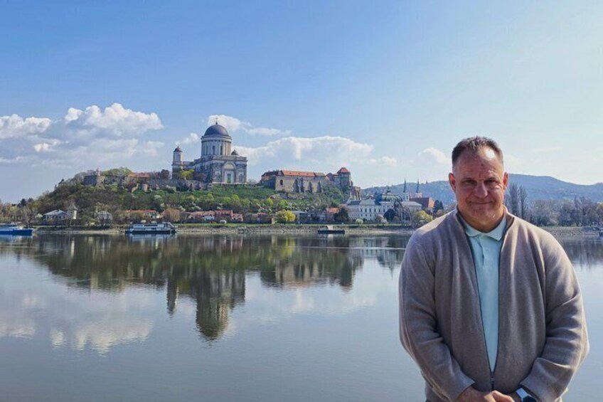 A man standing by a calm lake with a historic building and a dome in the background. 3