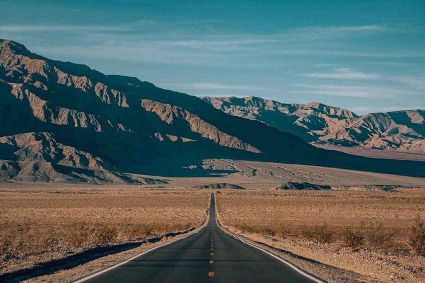 A straight road leading through a desert landscape with mountains in the background. 2