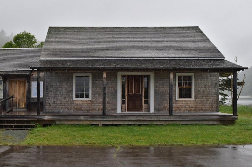 A rustic wooden building with a sloped roof, a front porch, and a small grassy area in front. 4