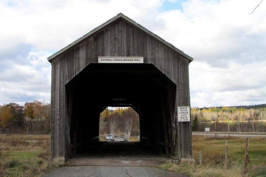 Eine gedeckte Brücke mit einem Schild, auf dem 'Sawmill Creek Bridge 1905' steht, und einem Warnschild zur Sicherheit von Pferden. 2