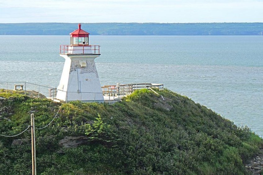 A lighthouse on a grassy hill overlooking a calm body of water. 2