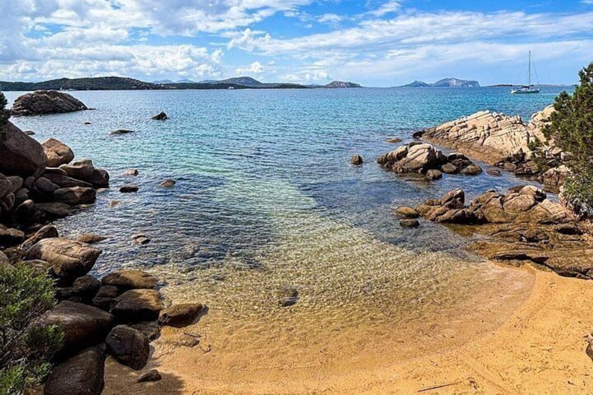 A coastal landscape with clear water, rocks, and a distant sailboat. 2