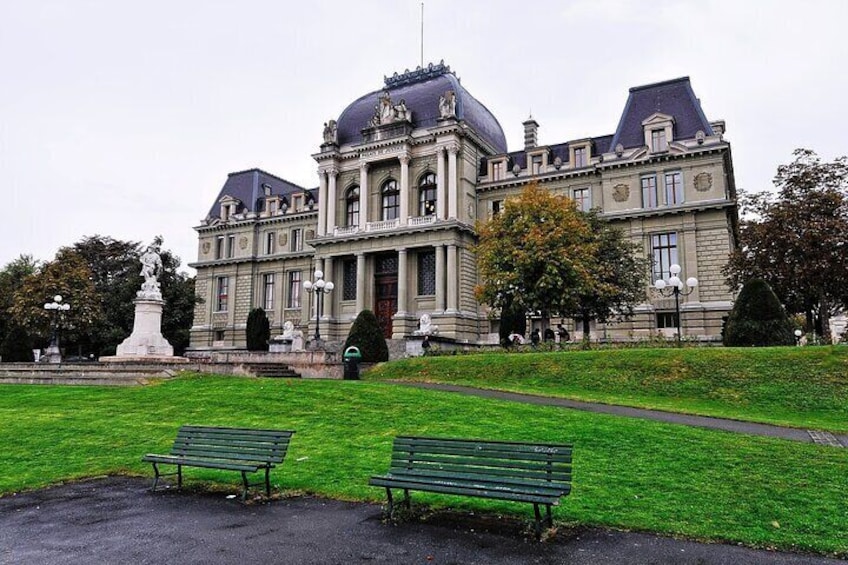 A large, historic building with a dome and columns, surrounded by a well-maintained lawn and two benches. 1