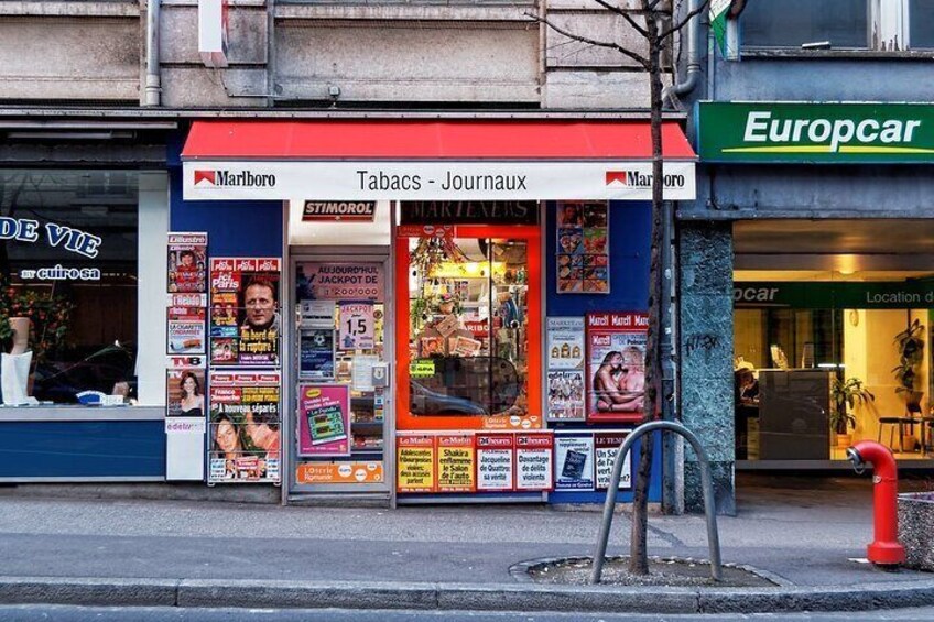 A tobacconist shop with a red awning and various advertisements. 2