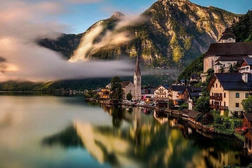 A lake with a mountain in the background, a church, and traditional houses. 1