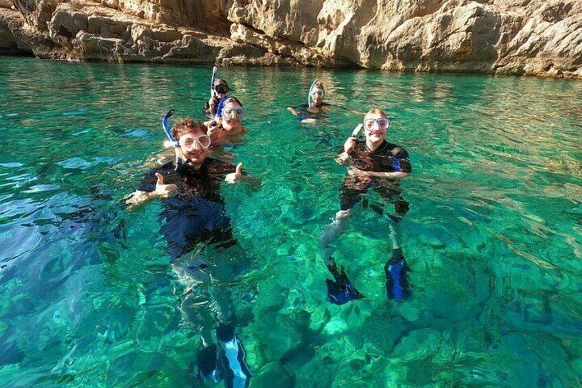 Personas haciendo snorkel en aguas cristalinas con acantilados rocosos al fondo. 1