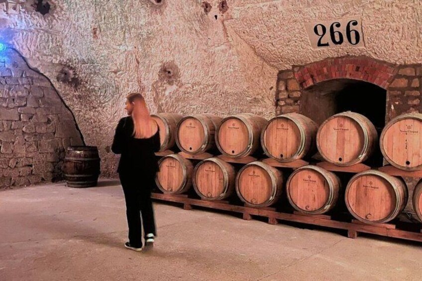 Una persona de pie frente a barriles de madera, con un muro de piedra y un horno de ladrillo al fondo. 5