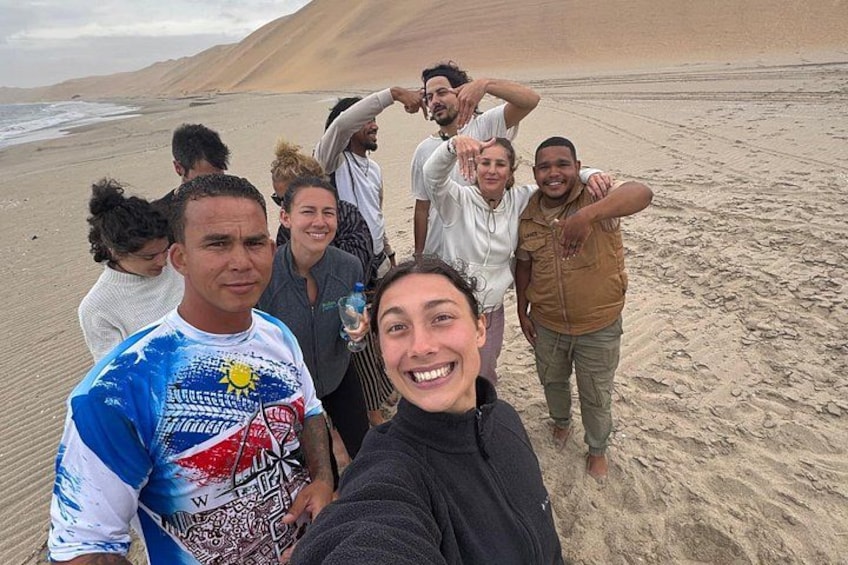 Un grupo de personas en una playa arenosa con dunas al fondo. 4