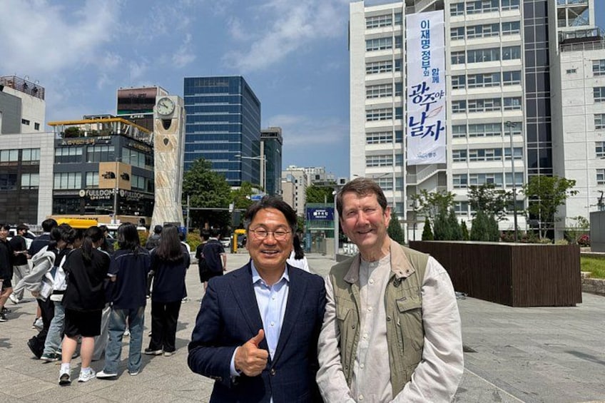 Two men in business attire standing in an urban plaza with modern buildings and a clock tower in the background. 5
