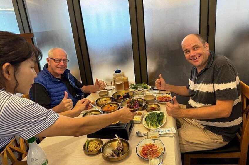 A group of people sitting around a table with various dishes and a bottle of water. 3