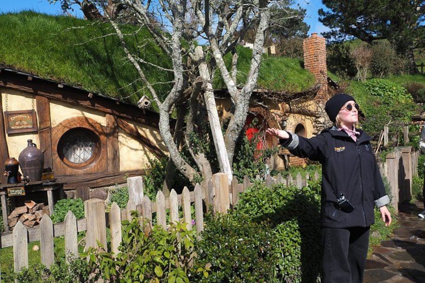 Eine Person in einem Kostüm steht vor einem Haus im Hobbit-Stil mit einem Holzzaun. 2