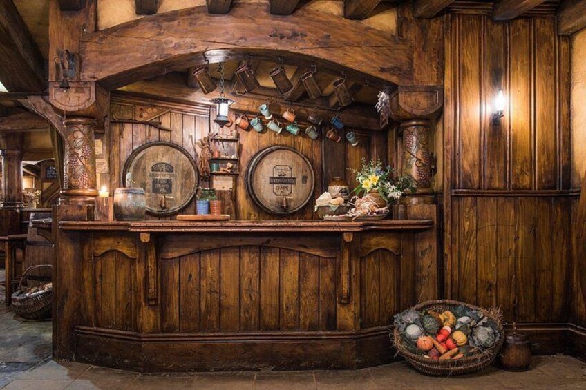 Eine Holztheke mit zwei großen Fässern, einem Obstkorb und einer hängenden Glocke. 5