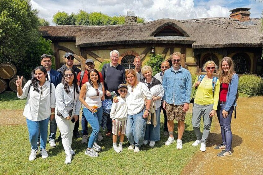 A group of people standing in front of a thatched-roof building with a rustic appearance. 4