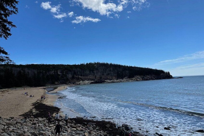 Una playa con costa rocosa, agua tranquila y un acantilado con bosque. 2