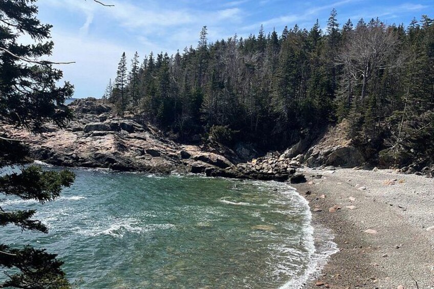 Un rivage rocheux bordé d’une eau claire, entouré d’une forêt dense. 1