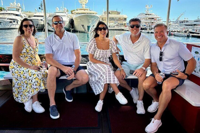 Un groupe de personnes se trouve sur un bateau, avec une marina et des yachts en arrière-plan. 4