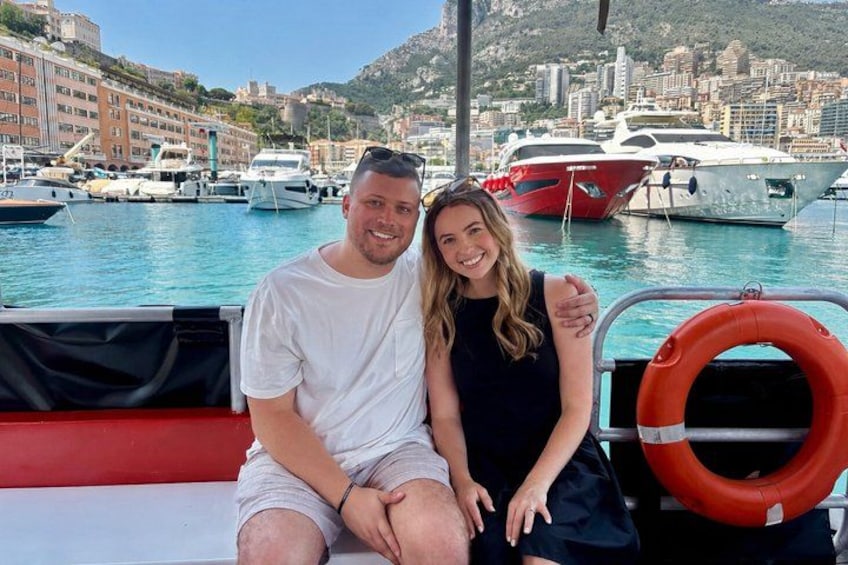 A couple on a boat with a marina and yachts in the background. 3