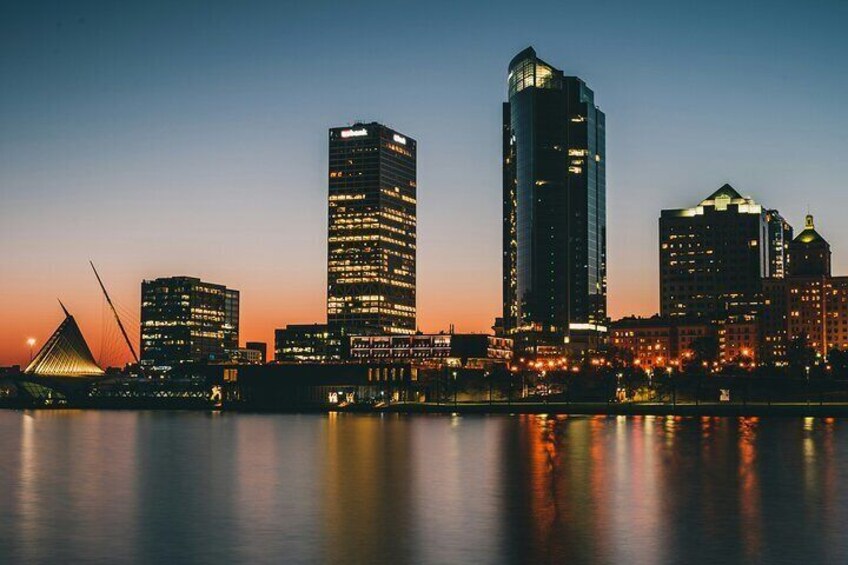 A city skyline at dusk with illuminated buildings and a bridge reflecting on the water. 2