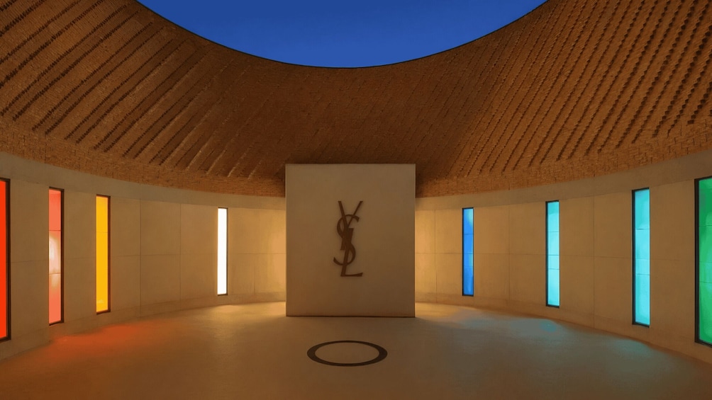 Un espacio interior con techo de madera, una escultura central y paredes con vidrieras de colores. 2