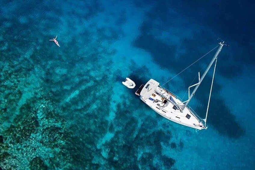 A white sailboat anchored in clear blue waters with coral reefs visible beneath the surface. 2