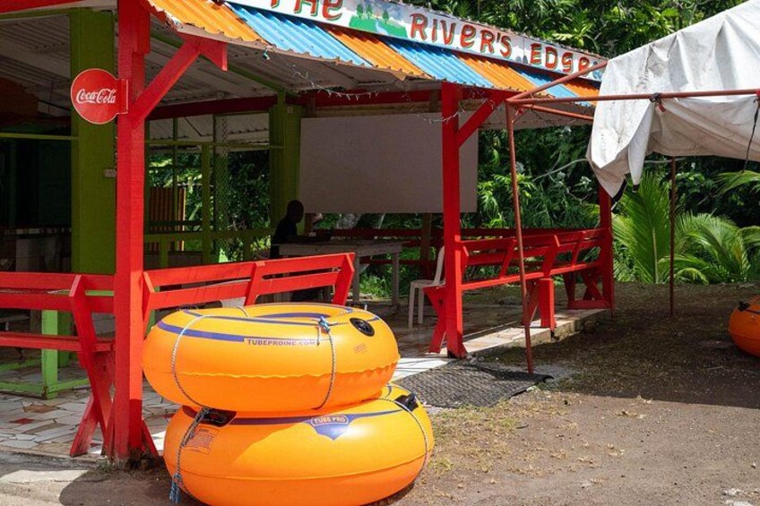 A riverside eatery with a Coca-Cola sign, outdoor seating, and two inflatable tubes. 4