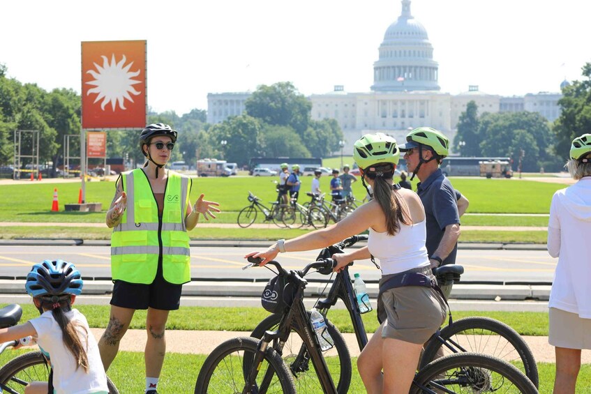 A group of cyclists in a park with a large building in the background. 5