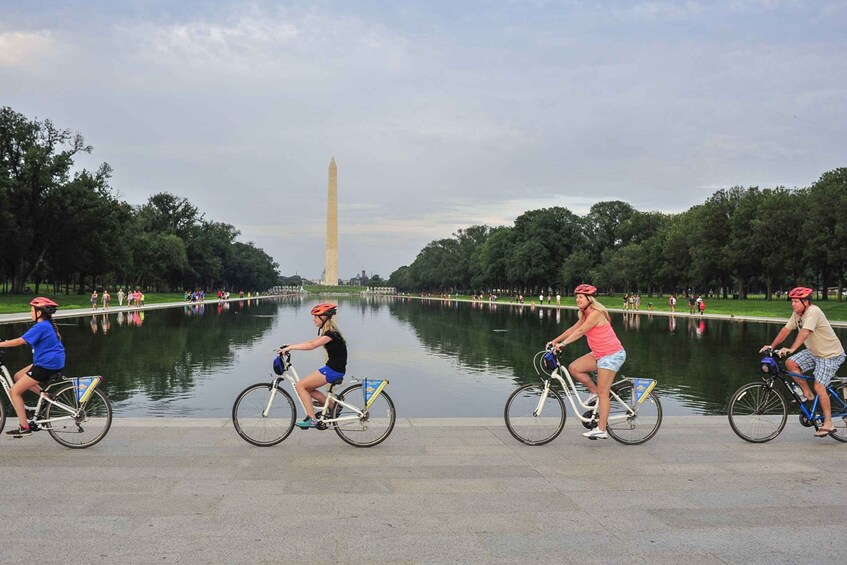 People riding bicycles along a path with a large monument in the background. 1