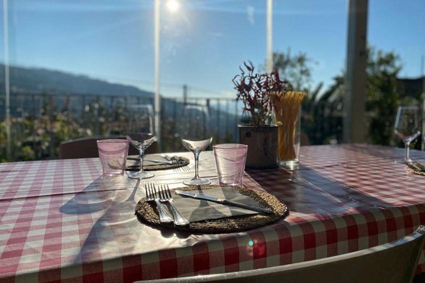 A table set for dining with a checkered tablecloth, a vase with dried flowers, and a view of a mountainous landscape. 4