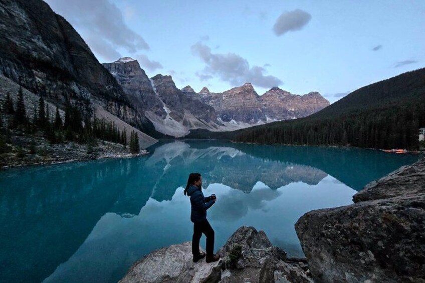A person standing on a rock by a clear lake with mountains in the background. 2