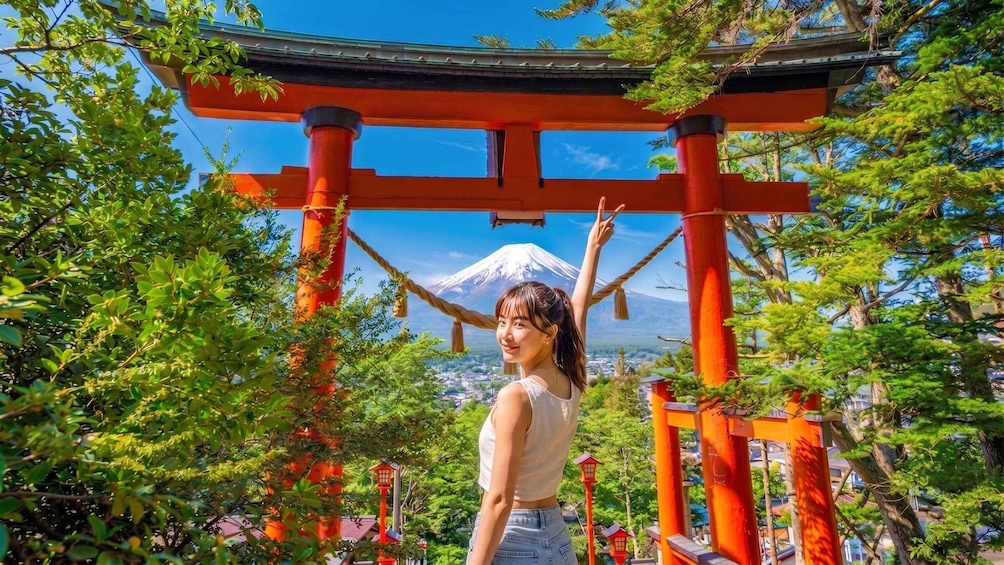 A person standing under a red torii gate with Mount Fuji in the background. 1