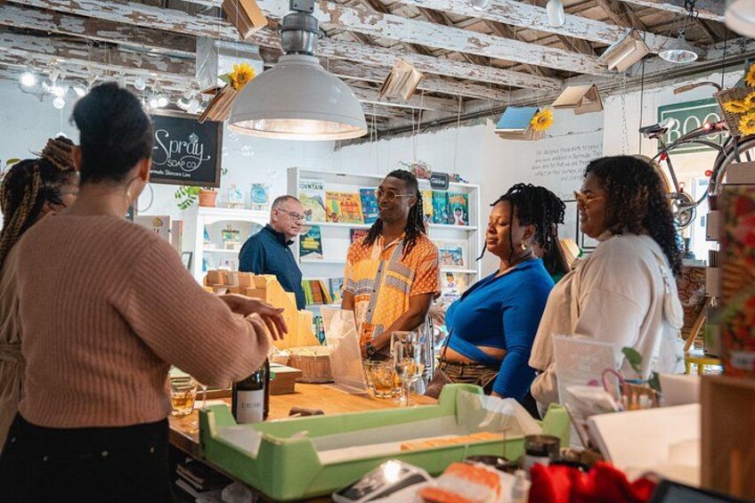 A group of people at a counter in a store with a rustic interior, including exposed beams and a hanging light fixture. 2