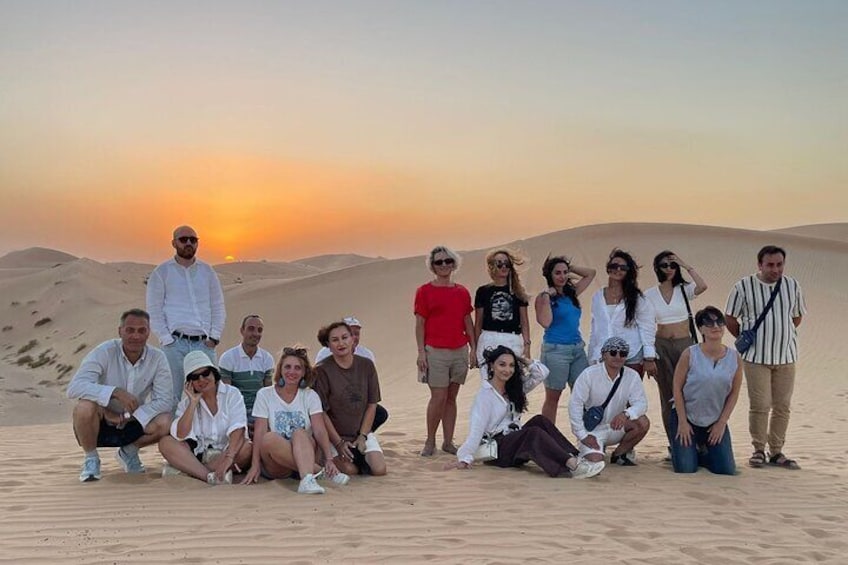 A group of people posing on a desert sand dune at sunset. 1