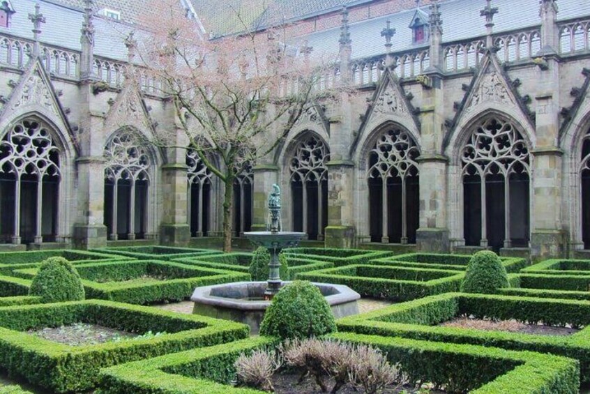 Un patio con una fuente, setos bien cuidados y arquitectura gótica. 1