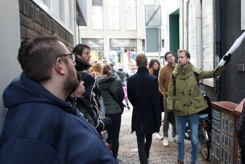 Un grupo de personas caminando por una calle adoquinada, algunas observando una pared con letreros. 4