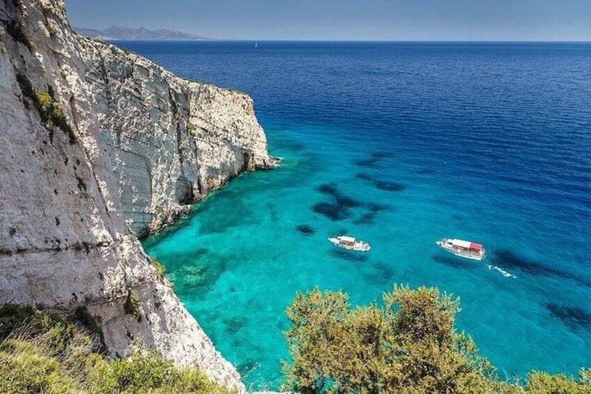 A coastal cliff, clear turquoise sea, and two boats. 3