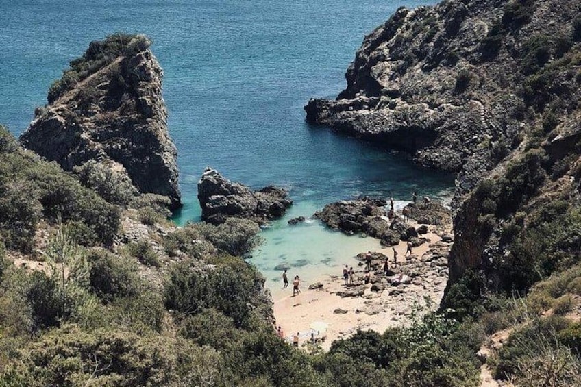 A coastal landscape with rocky cliffs, a sandy beach, and clear blue water. 2