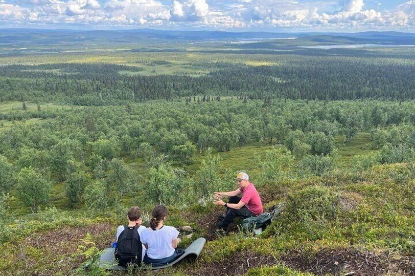 Three people sitting on a grassy hill overlooking a forested landscape. 2