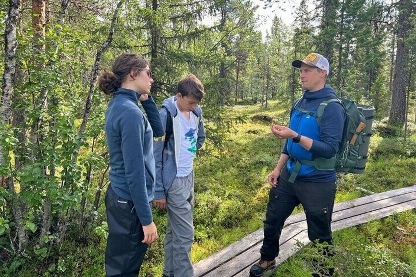 Three people standing on a wooden boardwalk in a forested area. 3