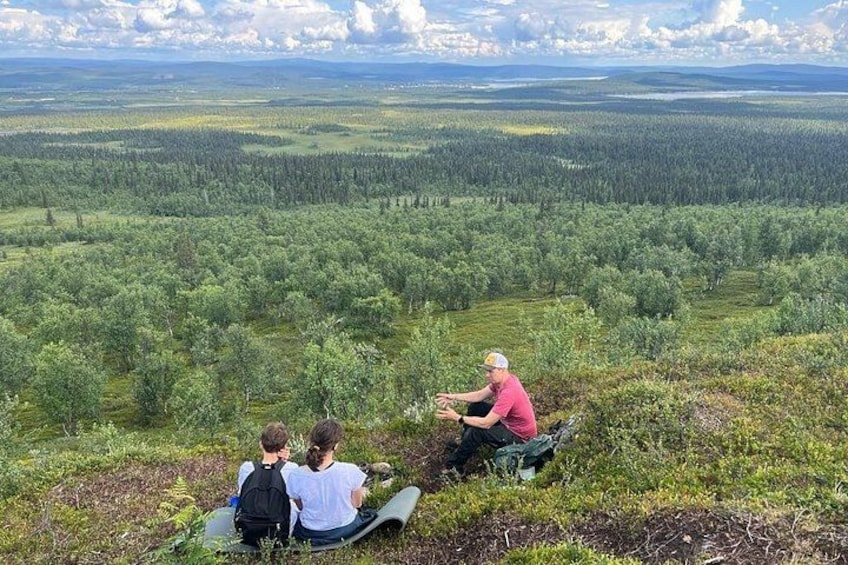 A group of people sitting on a grassy hill overlooking a forested landscape. 2