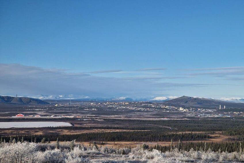 A vast landscape with a town in the distance, snow-covered trees, and mountains in the background. 1