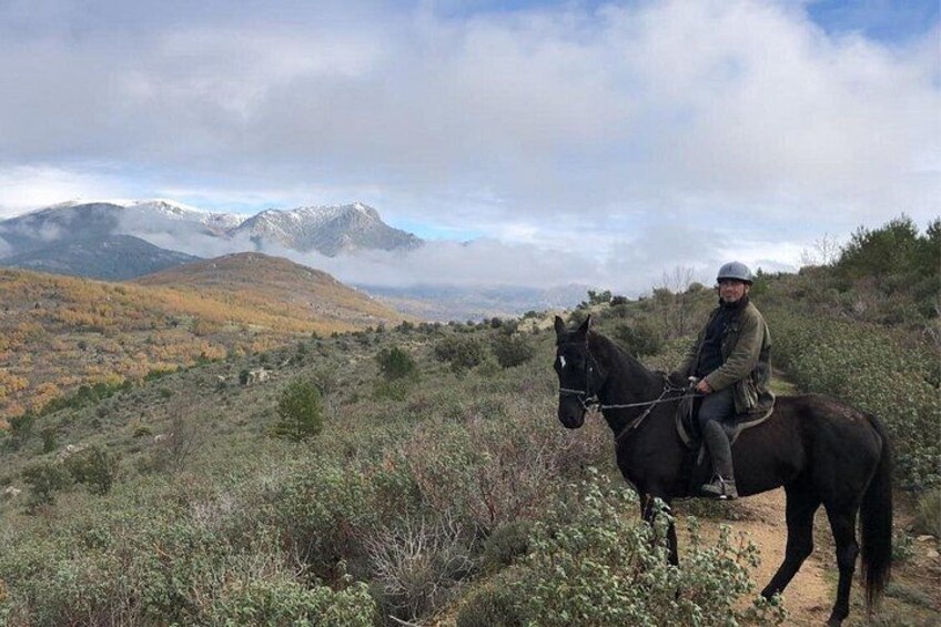 A person riding a horse on a mountain trail with autumn foliage and distant snow-capped peaks. 2