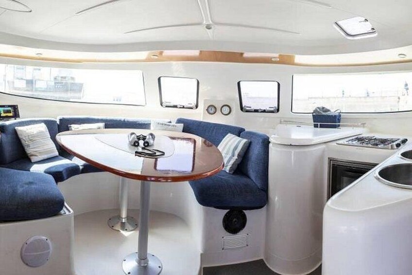 En lyxig inredning i en yacht med ett runt bord, blå klädda sittplatser och ett pentry med en spis. 4