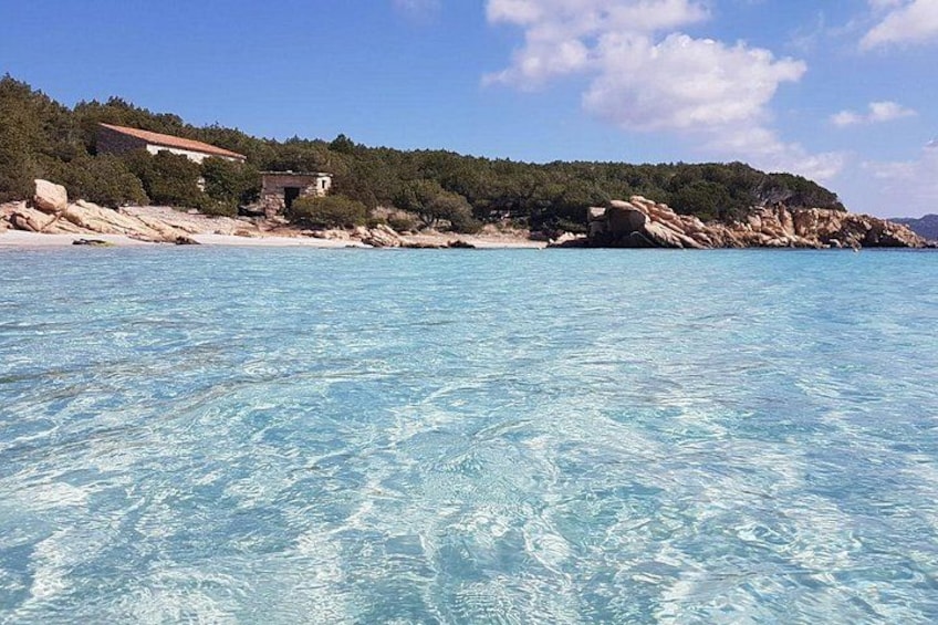 A clear blue sea, rocky coastline, and buildings on a hillside. 2