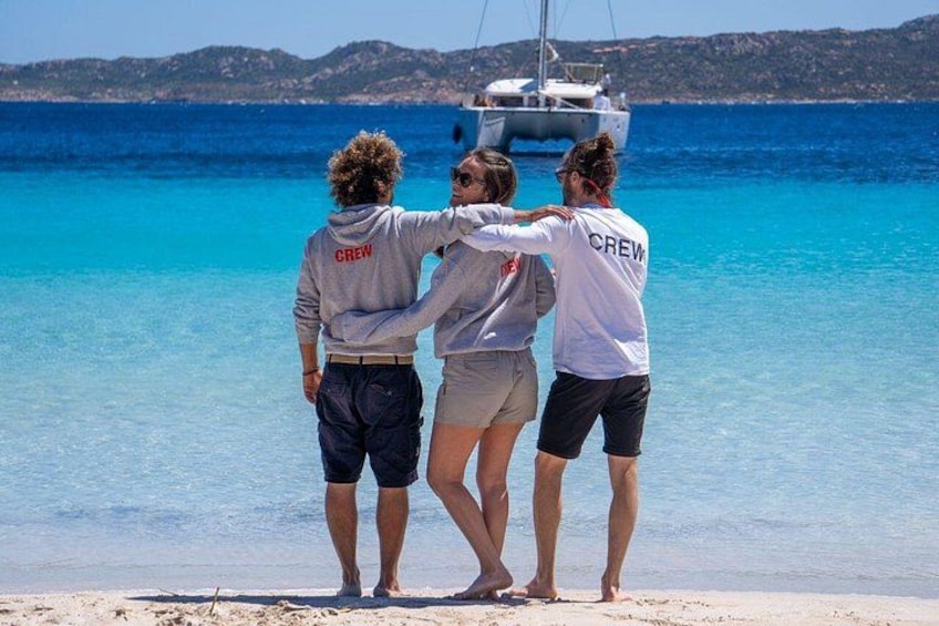 Trois personnes se tiennent sur une plage, avec un bateau en arrière-plan. 5