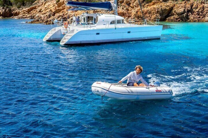 A person on a small inflatable boat in clear blue water, with a larger boat in the background. 3